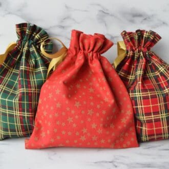 From left to right - small green tartan christmas fabric gift bag, small red christmas fabric gift bag with gold stars, small red tartan christmas fabric gift bag