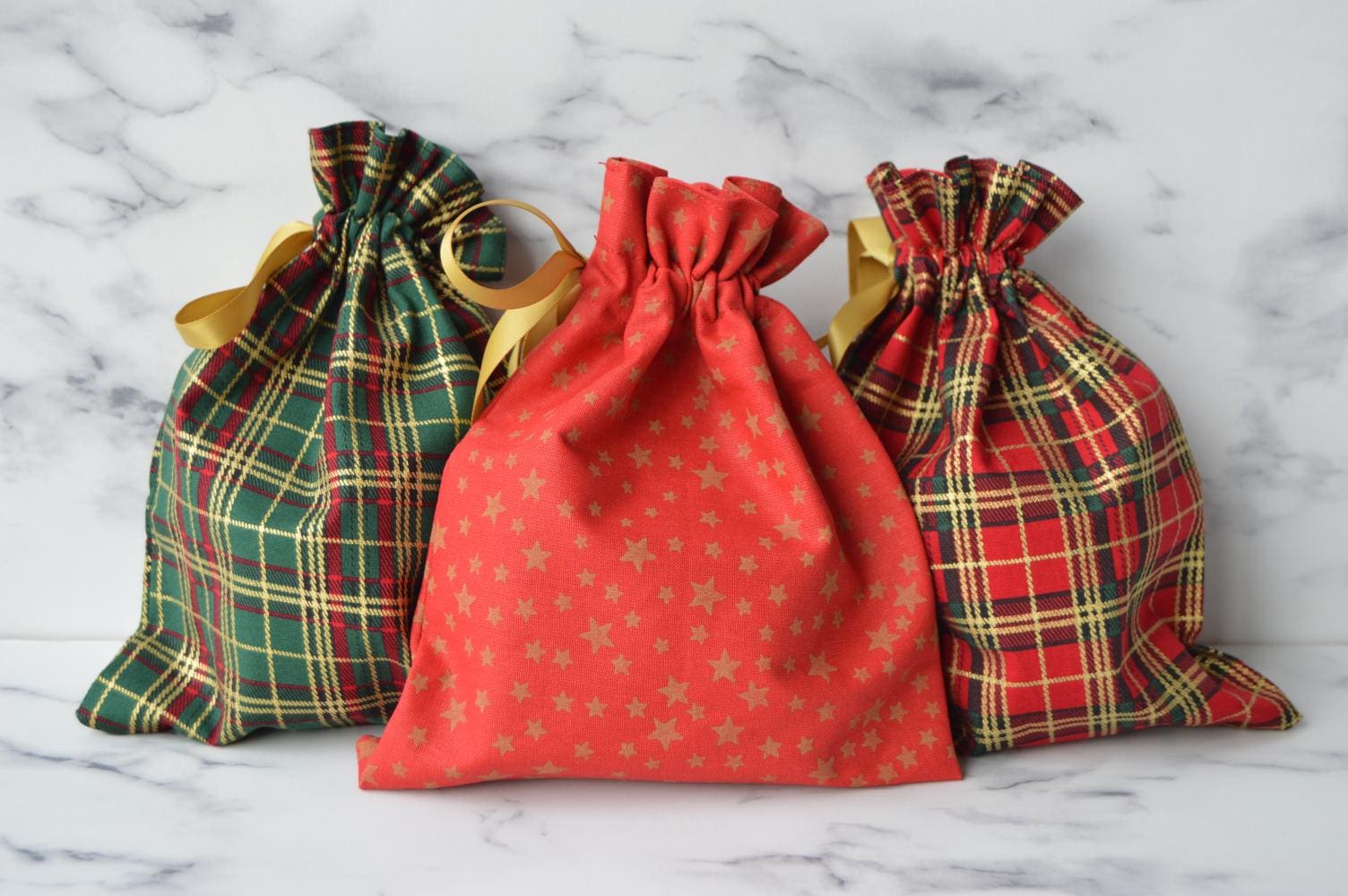 From left to right - small green tartan christmas fabric gift bag, small red christmas fabric gift bag with gold stars, small red tartan christmas fabric gift bag