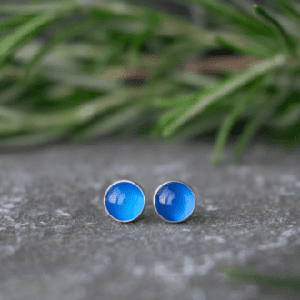 blue onyx gemstone stud earrings in sterling silver. Earrings rest on slate with foliage in background.