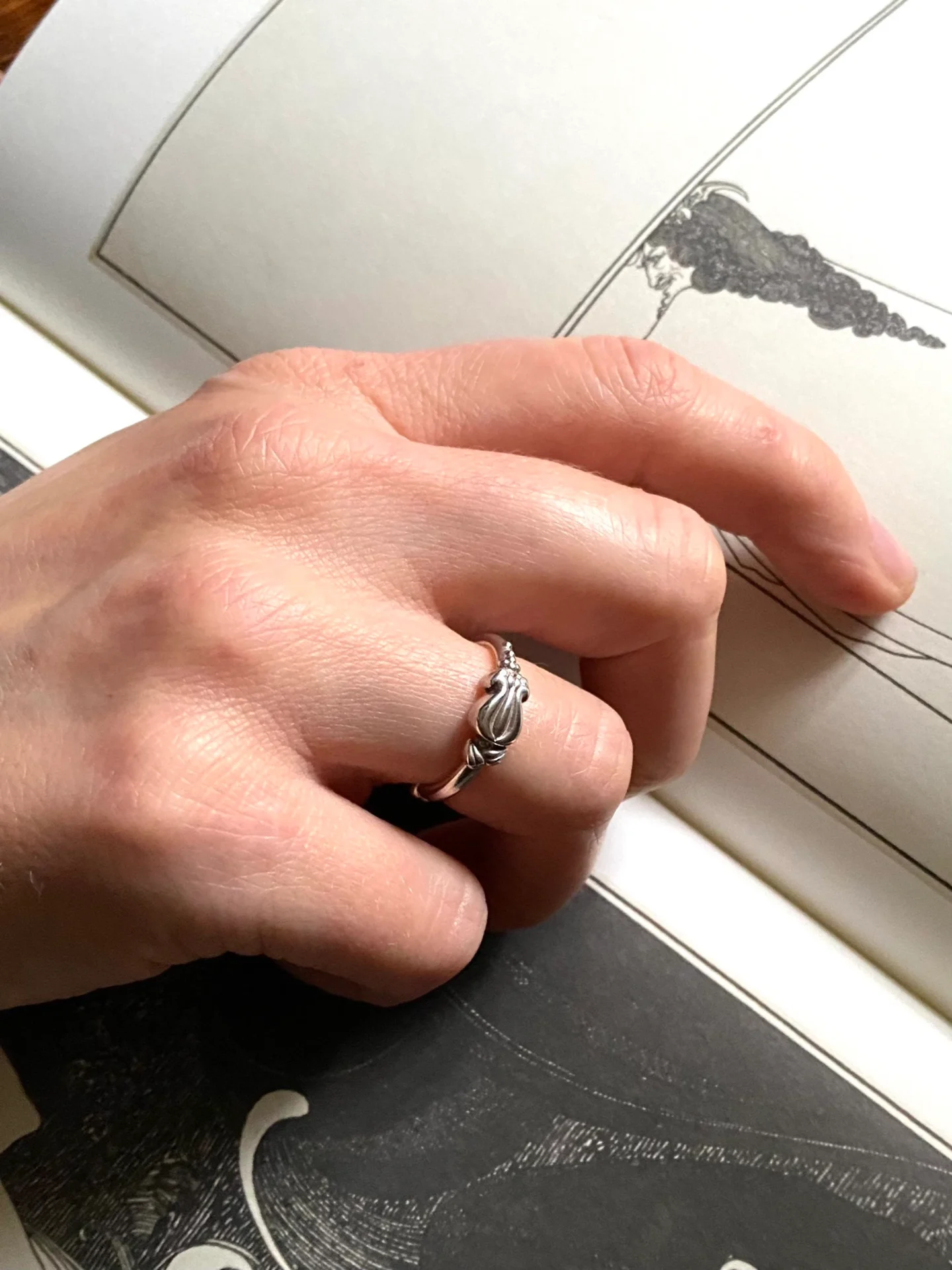 a hand is wearing a delicate silver ring with a flowery bud pattern