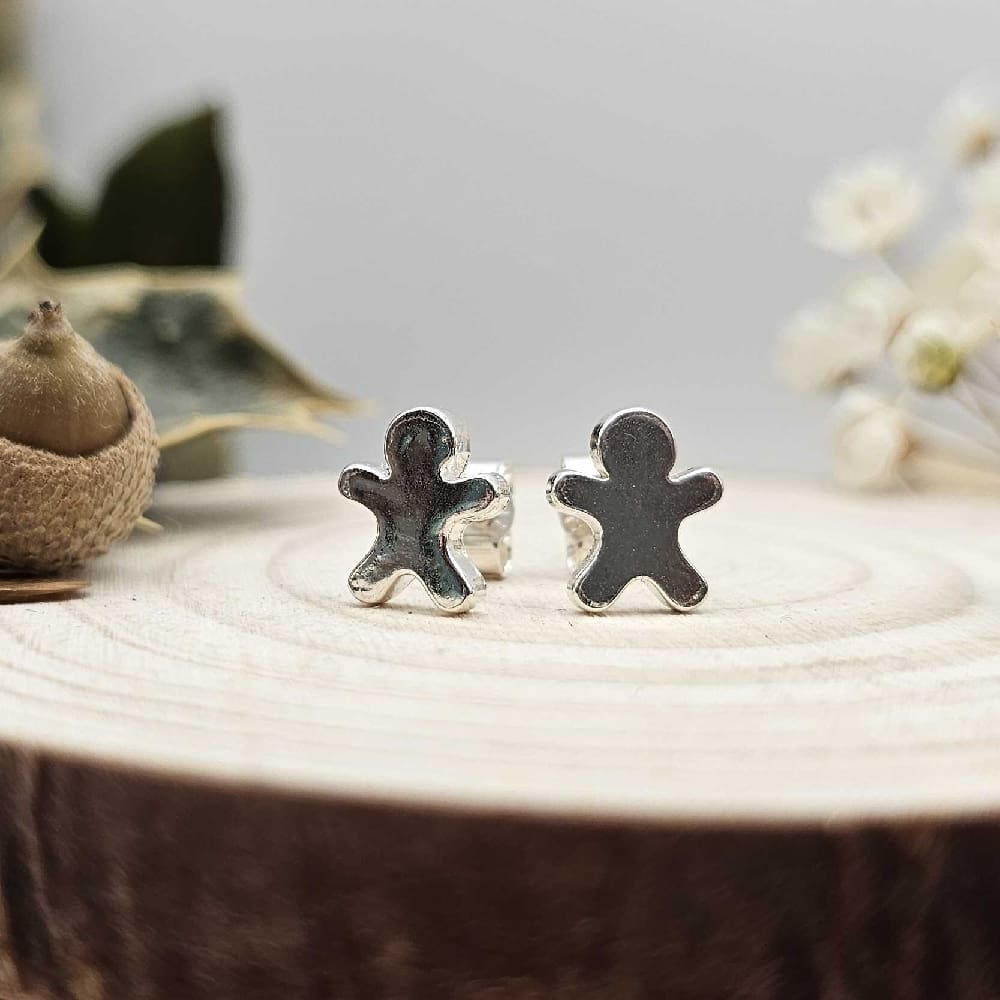 Pair of handcrafted recycled shiny sterling meeple gingerbread men shaped stud earrings sat on wooden disk