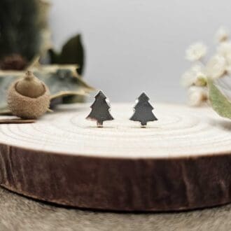 Pair of handcrafted recycled shiny sterling silver Christmas tree shaped stud earrings sat on wooden disk