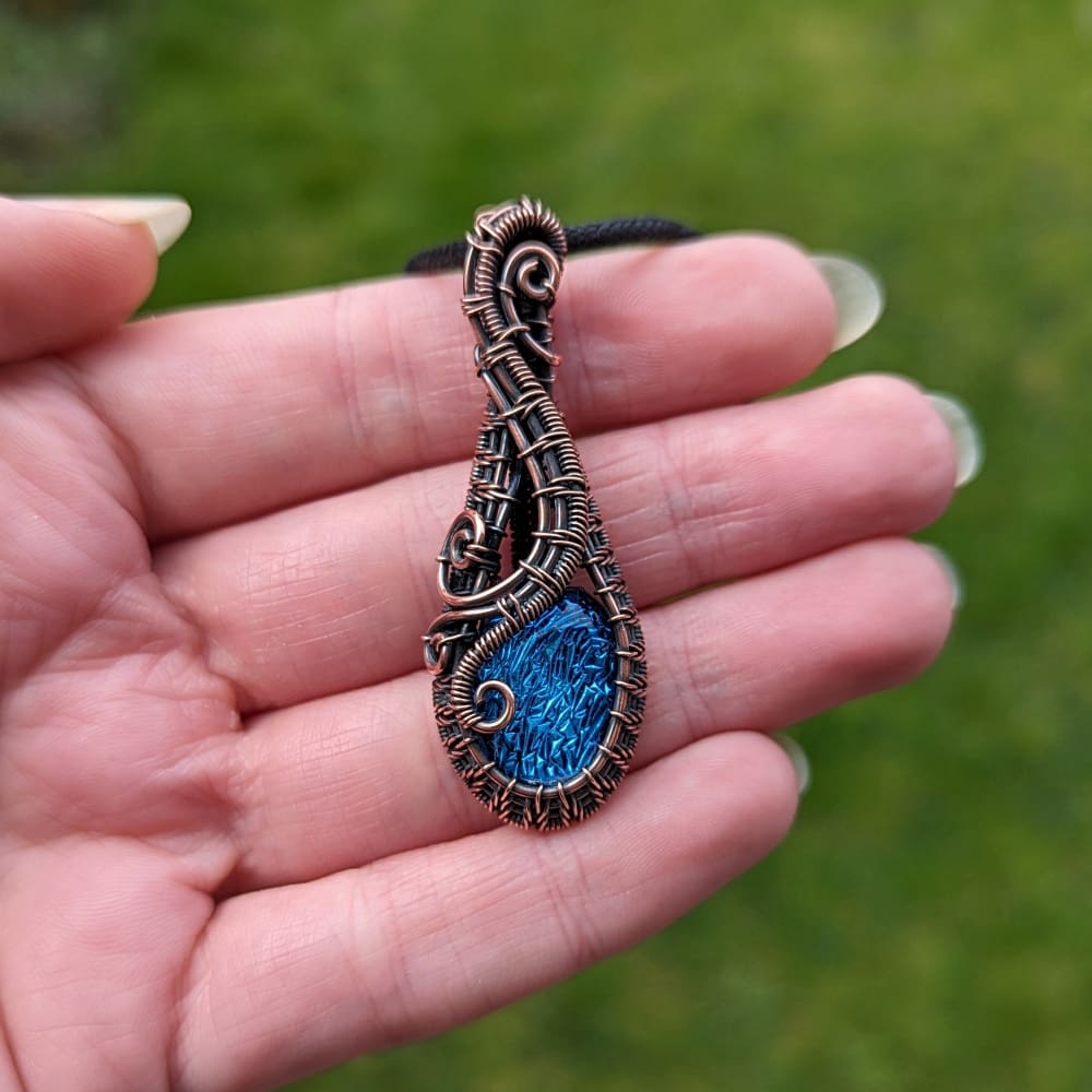 Hand holding a copper wire wrapped blue dichroic glass pendant