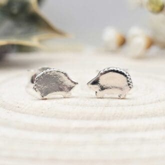 Pair of handcrafted recycled shiny sterling hedgehog shaped stud earrings sat on wooden disk