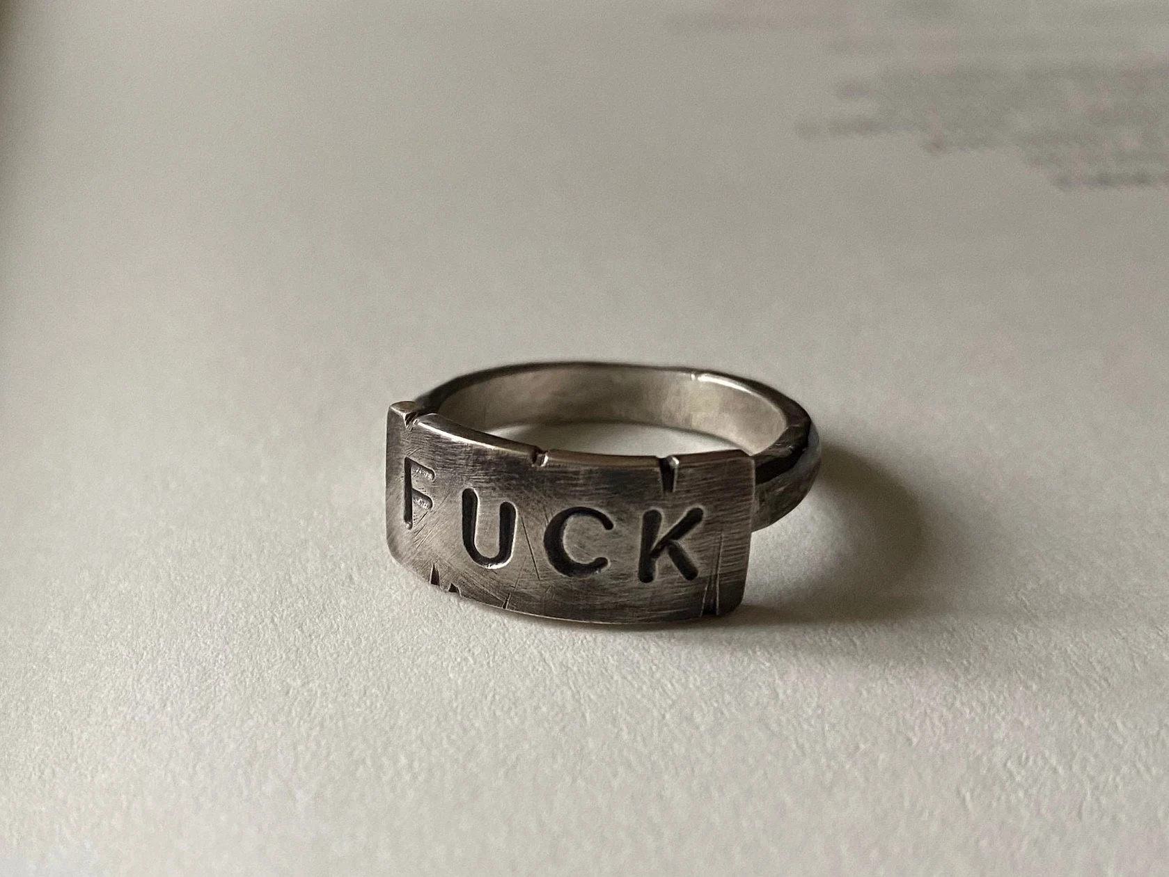 a silver ring with battered surface, and the word "FUCK" stamped on it.