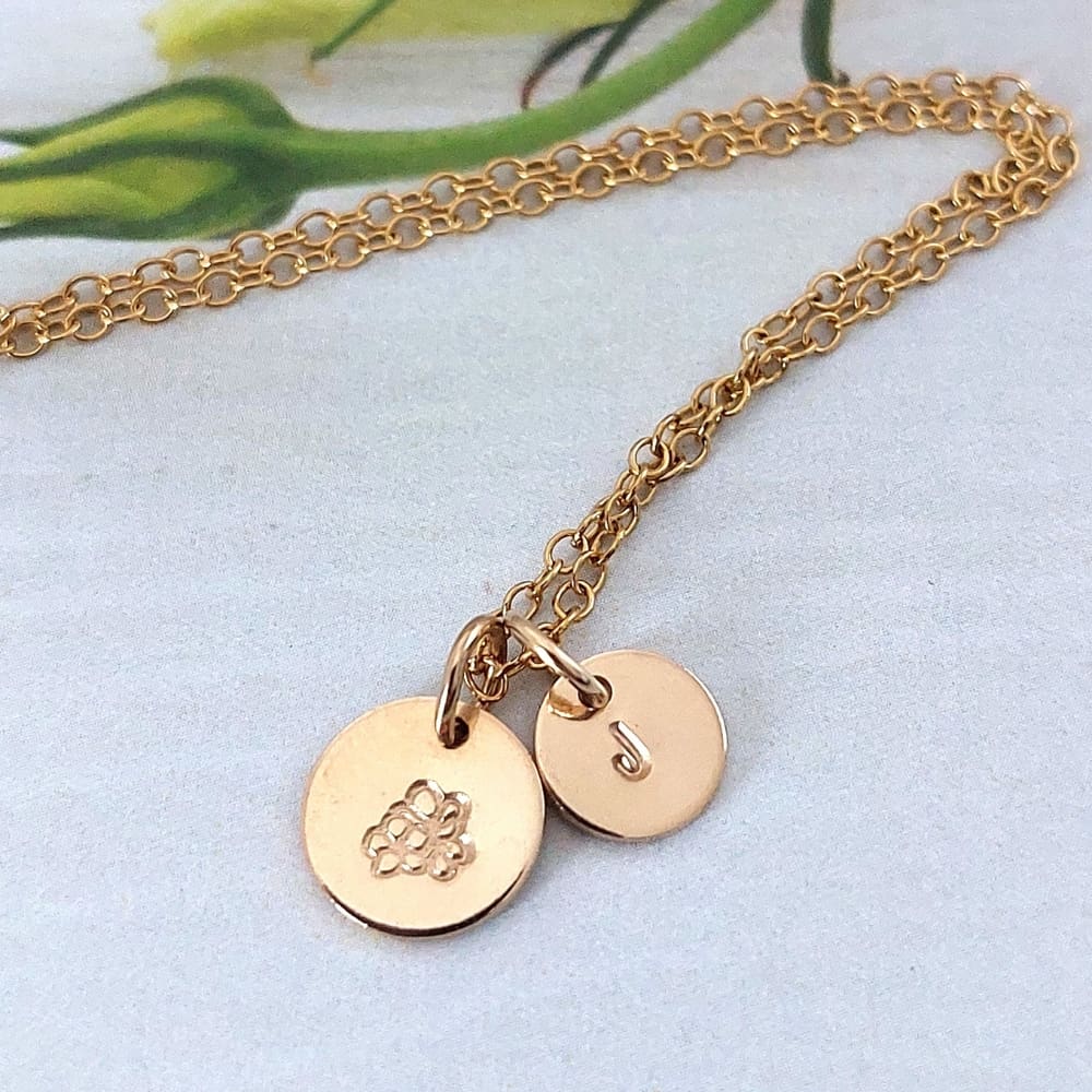 a 9mm disc featuring a hand-stamped birth flower design hanging on a gold filled trace chain necklace with an optional 7mm disc stamped with an initial