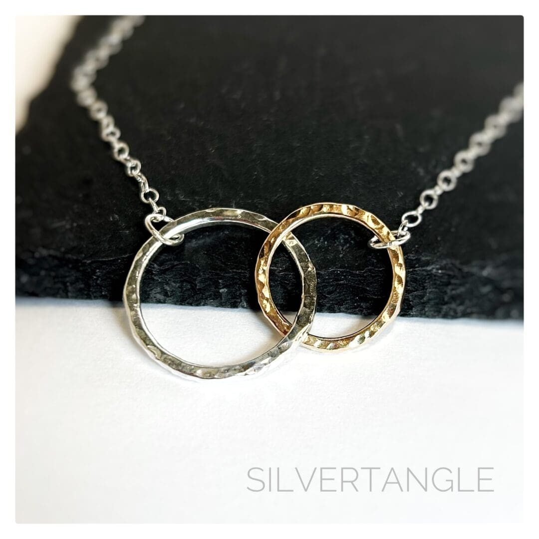 Necklace with two hammered rings interlocking, one gold and one silver joined to a silver cable chain sitting on a slate