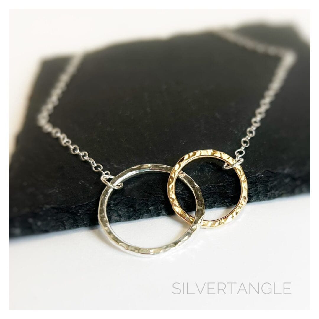 Necklace with two hammered rings interlocking, one gold and one silver joined to a silver cable chain sitting on a slate