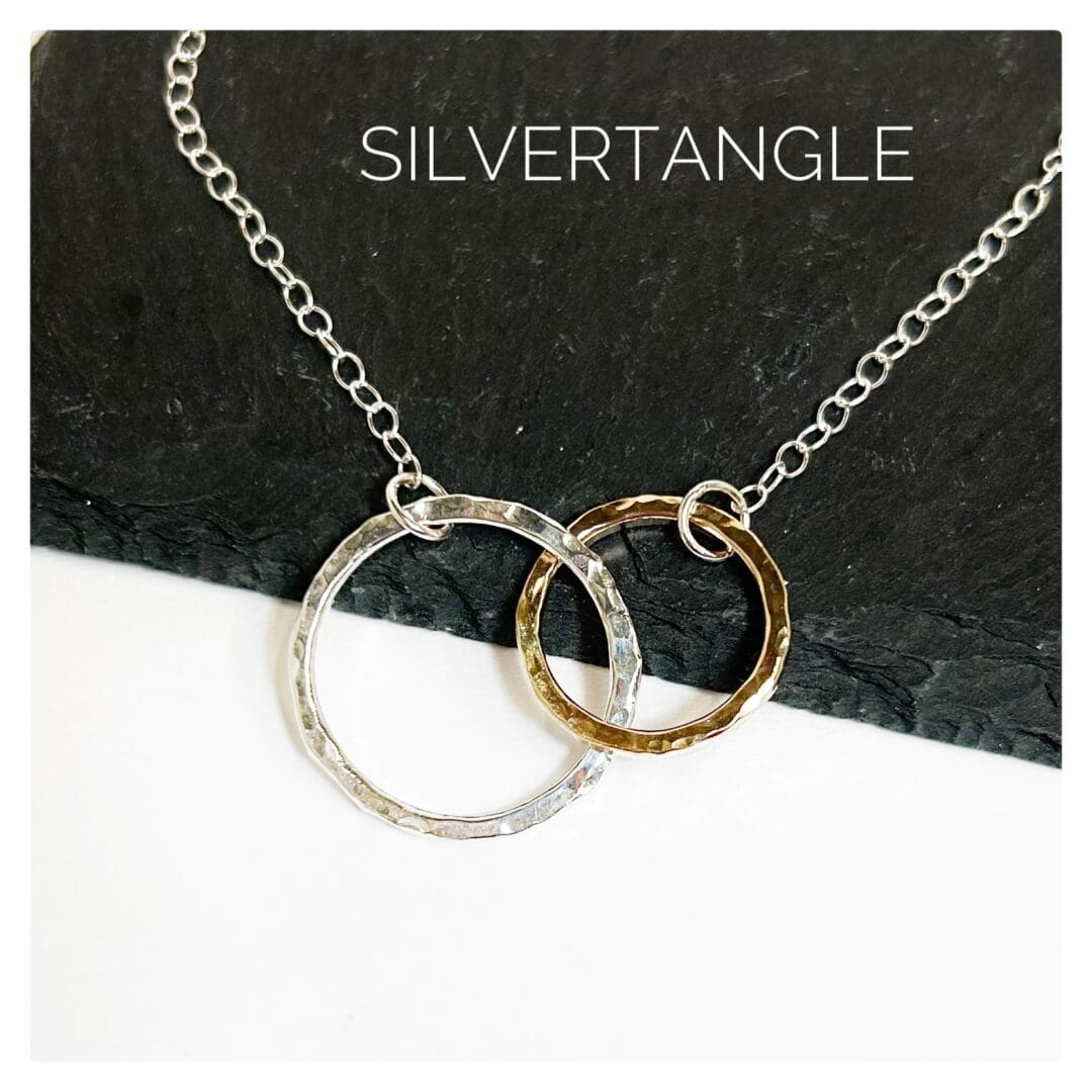 Necklace with two hammered rings interlocking, one gold and one silver joined to a silver cable chain sitting on a slate