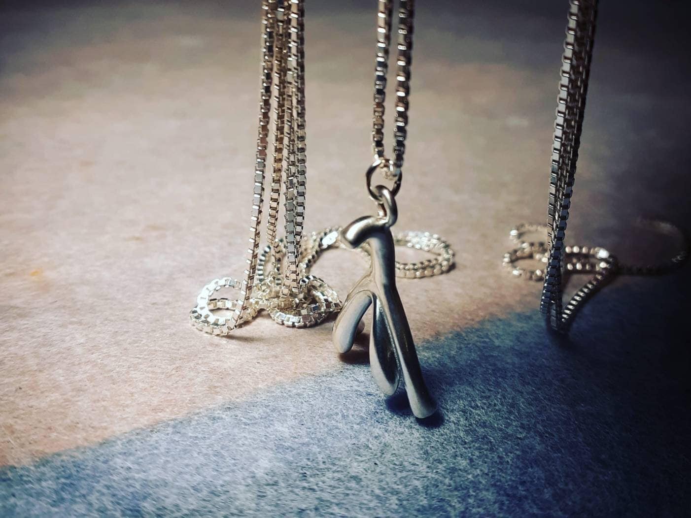 a pendant in the shape of the anatomical clitoris is hanging on a chain