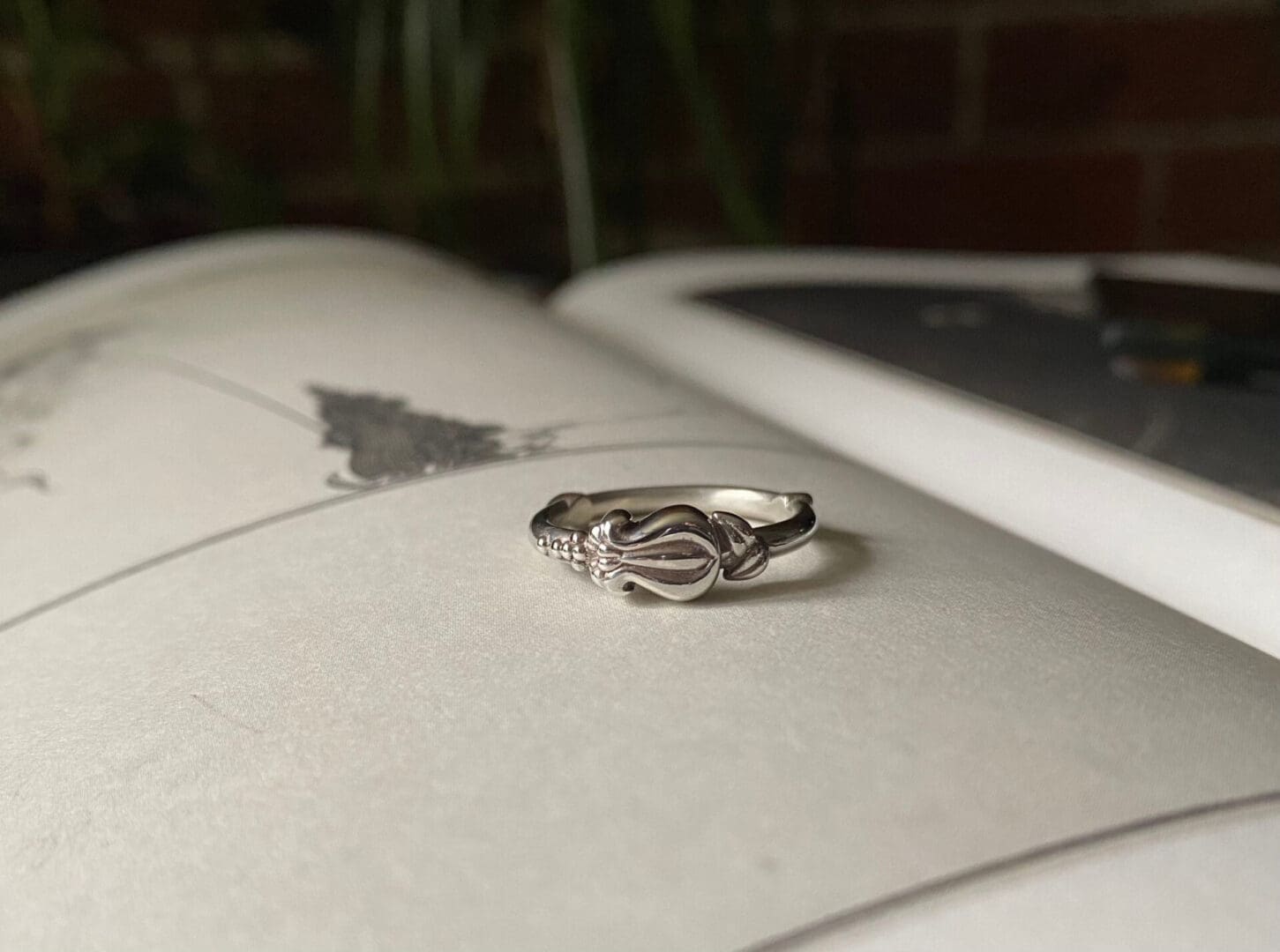 a silver ring with a small flower bud pattern lies on top of an open book. You can see parts of an art print on the page.