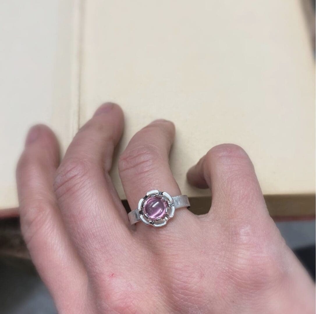 a hand is wearing a ring set with a pink stone.