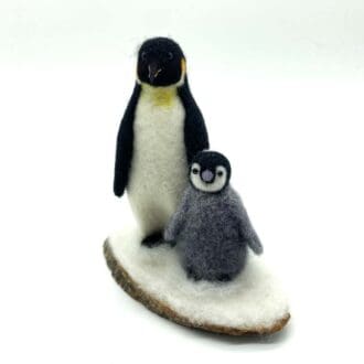 Front view of needle-felted penguin and chick sculpture, handcrafted with natural wool, displayed on a rustic wooden base