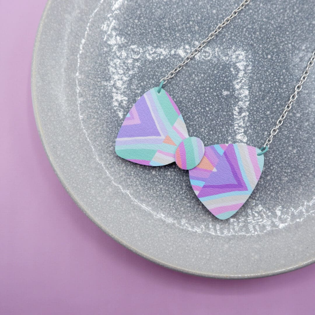 Cute bow shaped fabric and wood necklace. Pastel pinks, lilacs, peach and mint hand drawn striped material. Sat on grey speckled plate