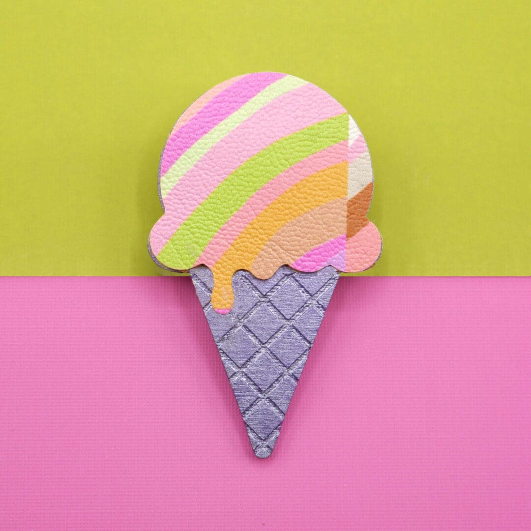 Handmade ice cream-shaped brooch with sorbet coloured stripes and a textured waffle cone, set against a bright green and pink colour-block background