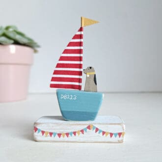 turquoise boat base and red and white stripe sail with a terrier dog sitting in the sailing boat