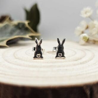 Pair of handcrafted recycled shiny sterling bunny rabbit shaped stud earrings sat on wooden disk