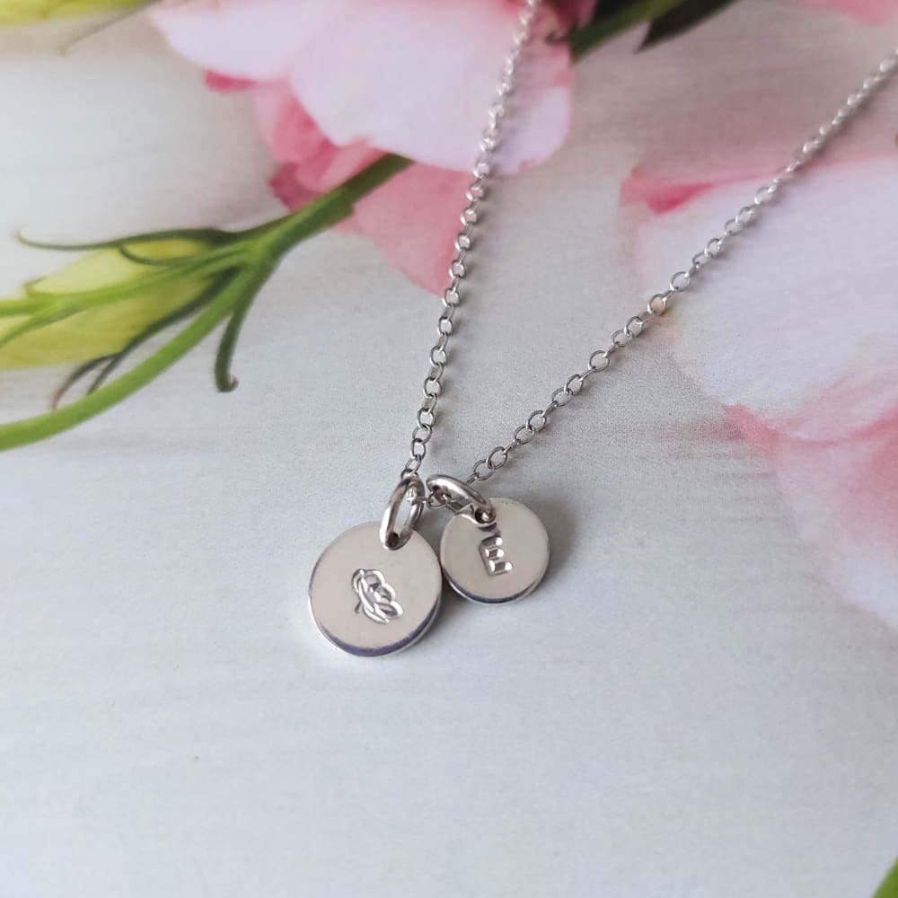 9mm silver disc hand-stamped with a zodiac sign alongside an optional 7mm stamped initial disc, on a silver trace chain necklace