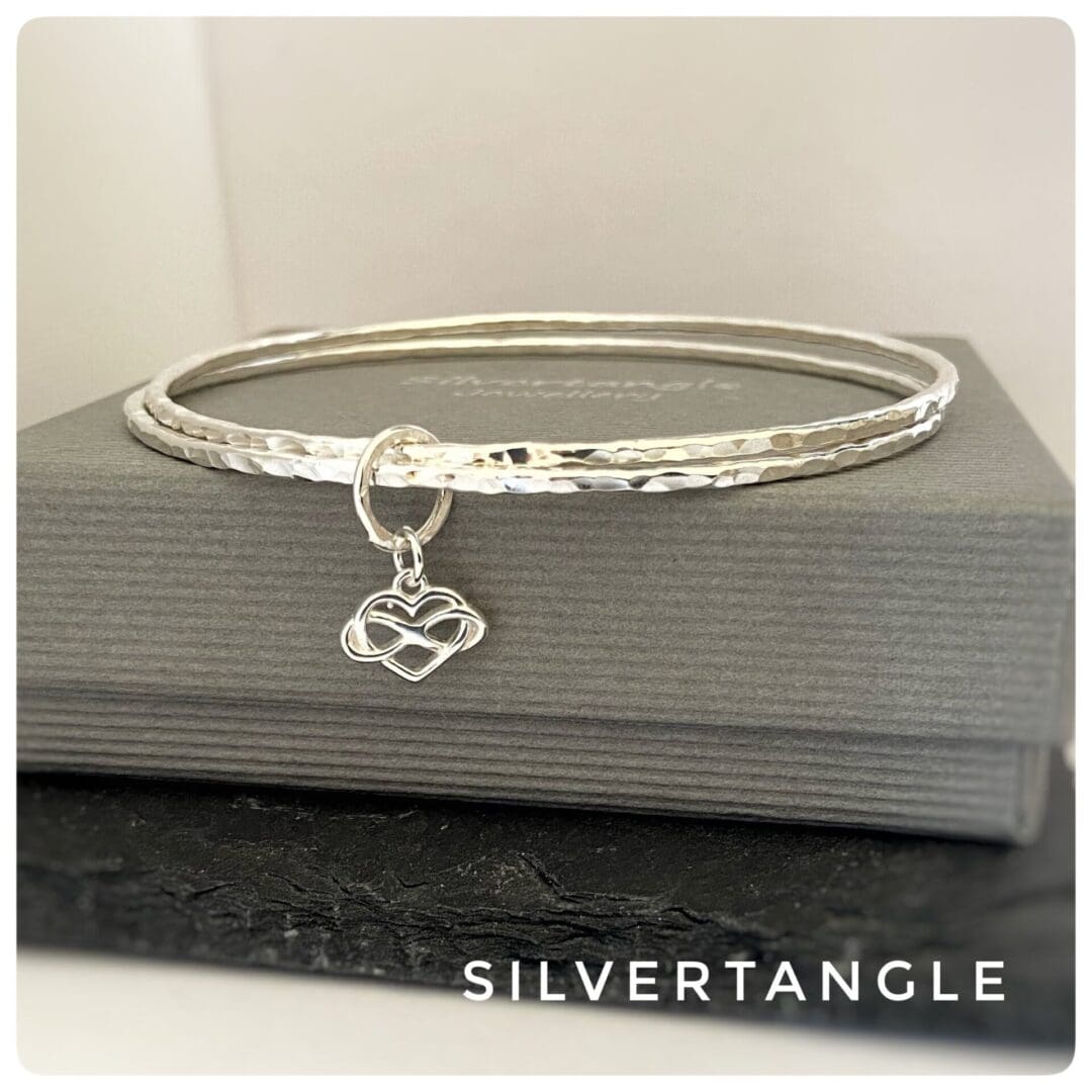 silver bangles with infinity heart charm on a grey box