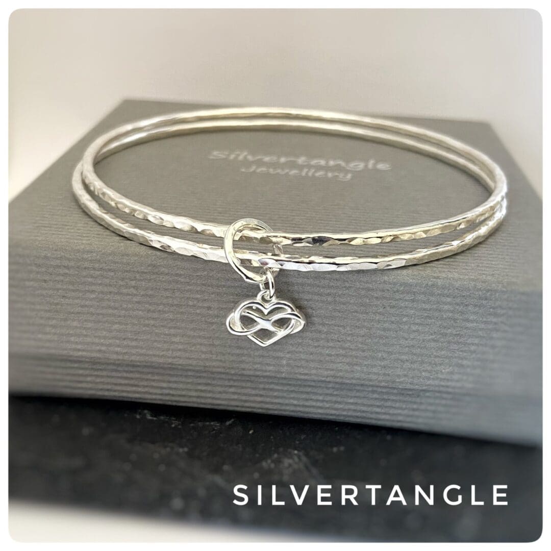 silver bangles with infinity heart charm on a grey box