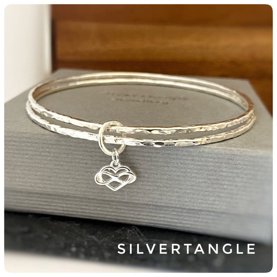 silver bangles with infinity heart charm on a grey box