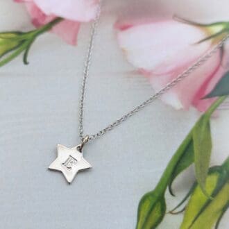 A 10mm silver star shaped pendant with a hand-stamped initial hangs from a sterling silver trace chain necklace