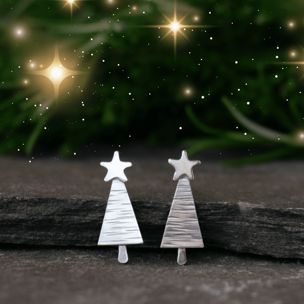 sterling silver christmas tree earrings resting on a slate with foliage in background