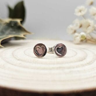 Displayed pair of handcrafted recycled sterling silver round stud earrings with hearts stamped in the centre