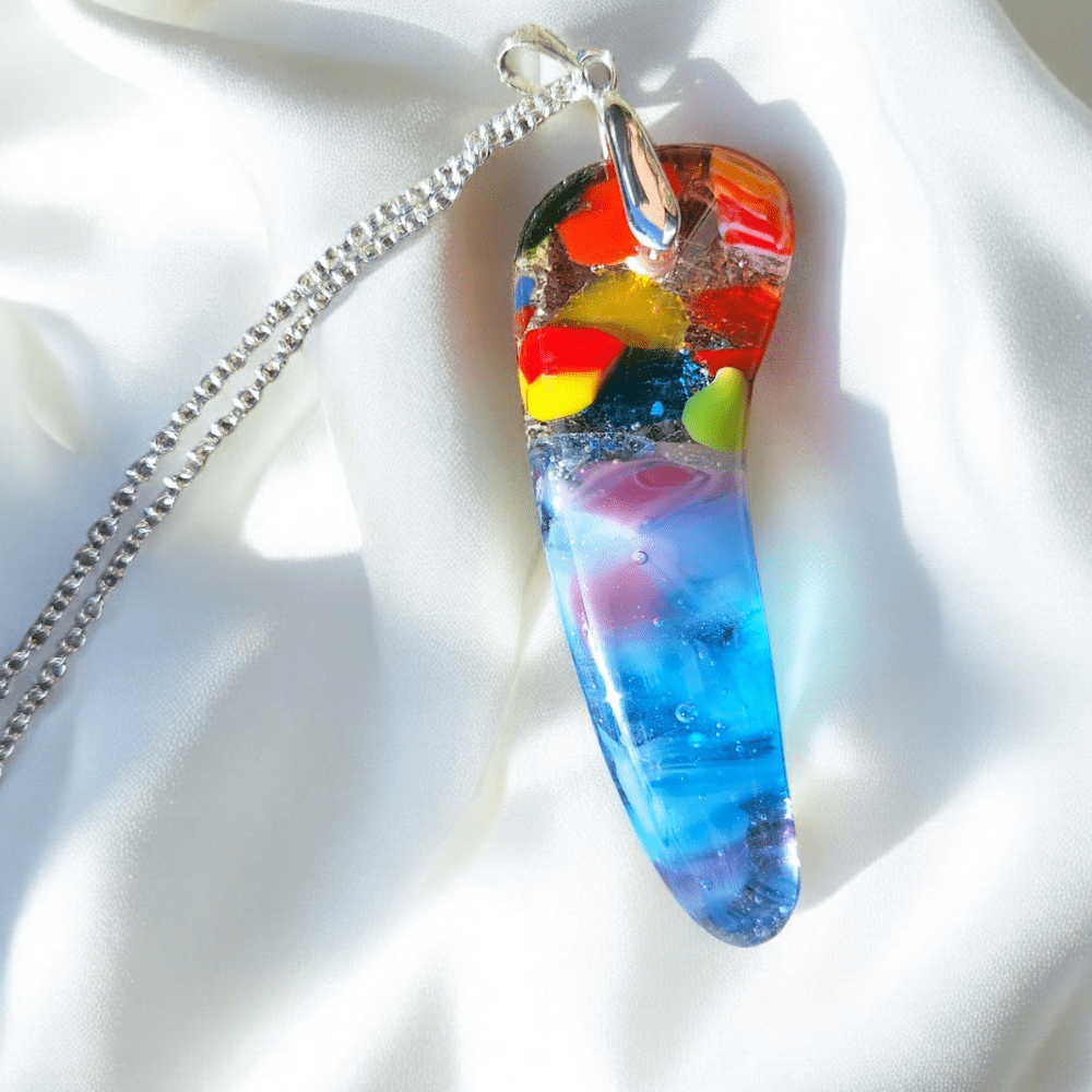 Bright and colourful fused glass pendant featuring rainbow colours and organic shapes, handmade with transparent glass, shown on a silver-plated chain against a white background. Ideal for unique jewellery lovers, festival glass fans, and those seeking unusual pendants or handmade jewellery gifts.