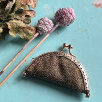 a small vintage feel needle case with a metal purse clasp fastener, sits on a wooden blue painted top surrounded by autumn leaves and seed pods