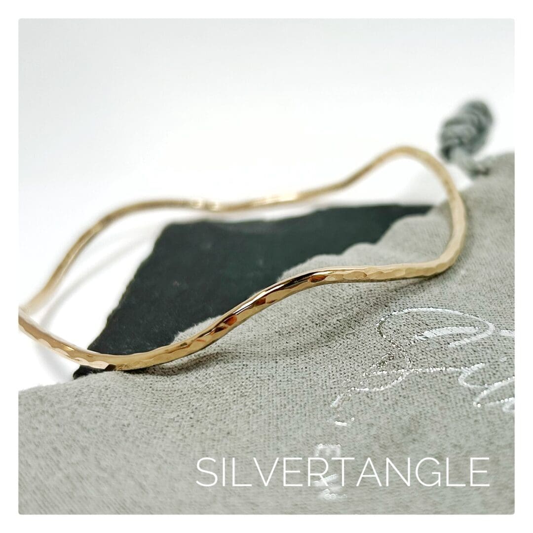 Wavy Hammered Gold Bangle sitting on a grey gift bag