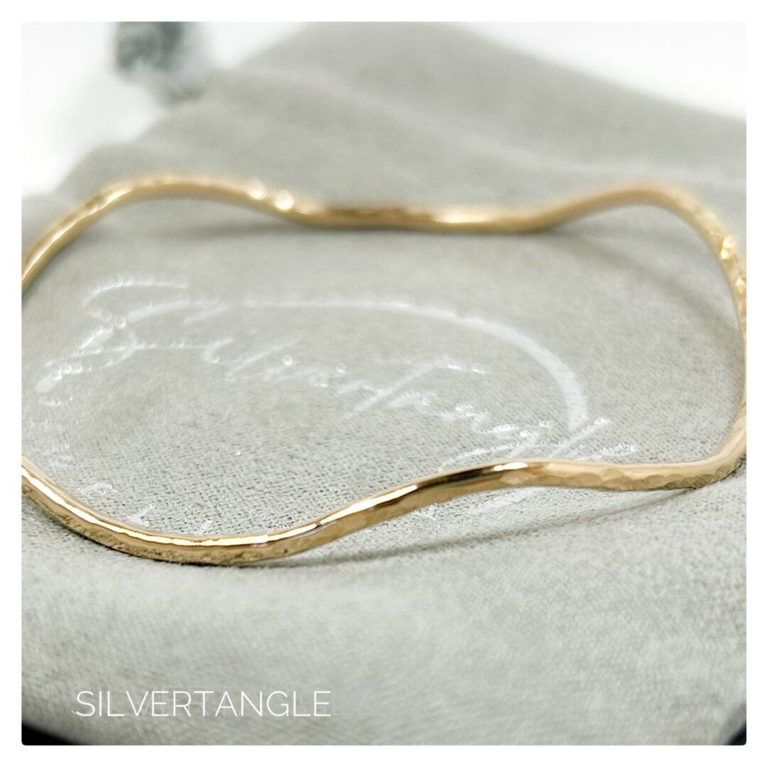 Wavy Hammered Gold Bangle sitting on a grey gift bag