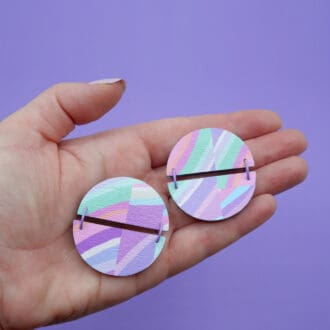 Unique pastel stripe patterned round studs. Made from 2 hinged semicircles. Held in white woman's hand