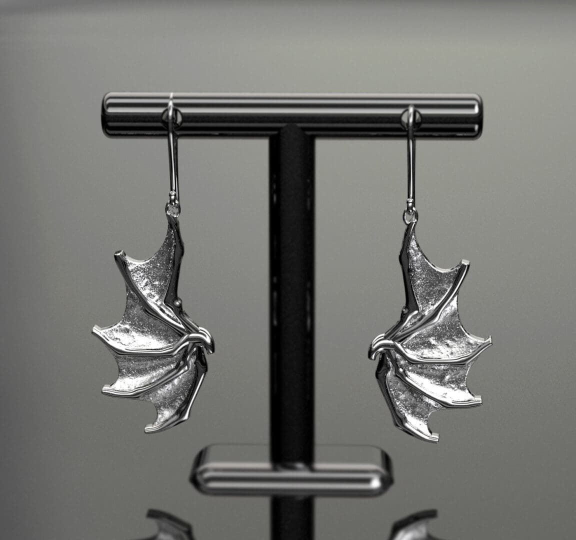 small silver earrings in the shape of dragon wings are hanging from an earring display stand. (CAD rendered image)