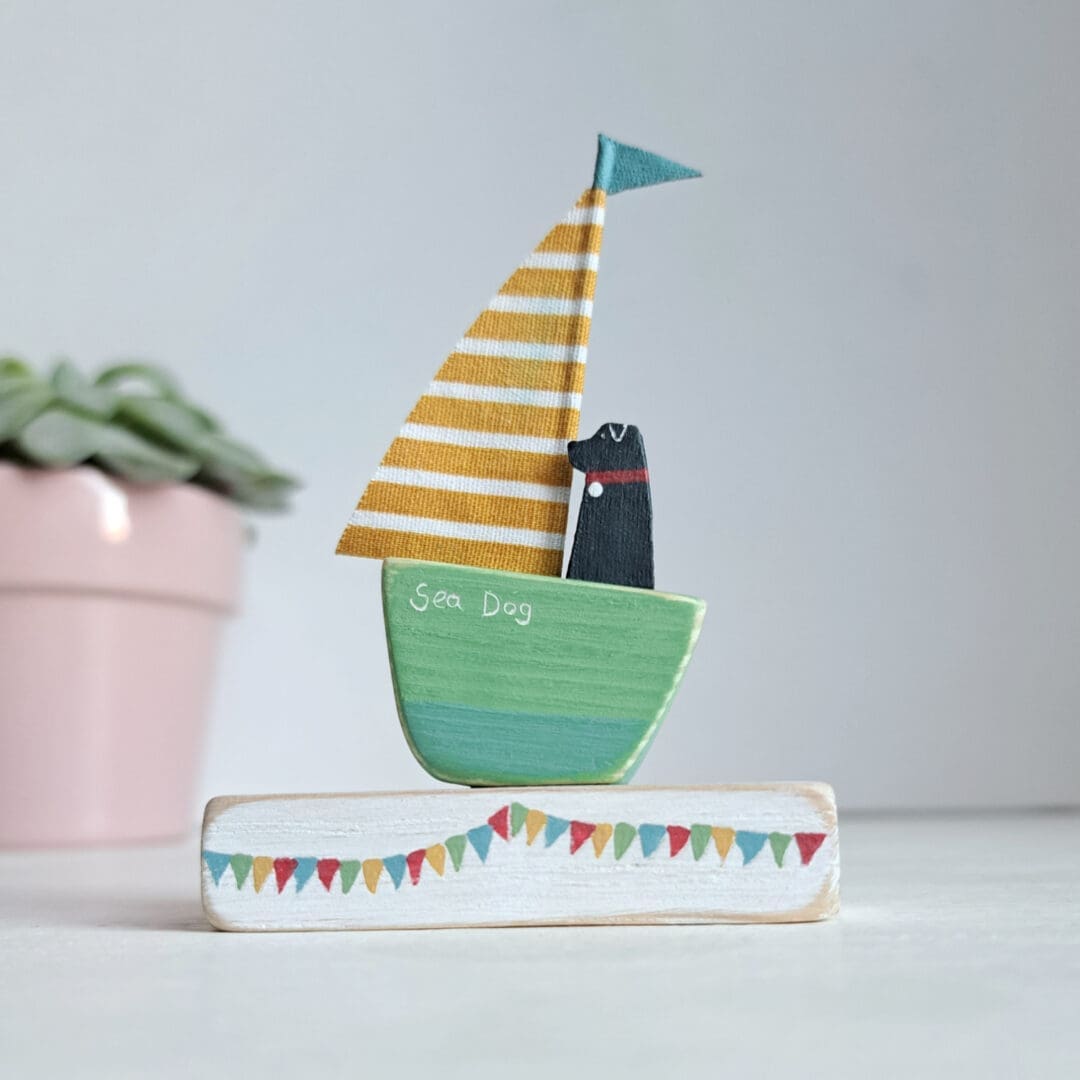 Sailing boat with green wooden base and yellow and white stripe sail with a black dog sitting in it