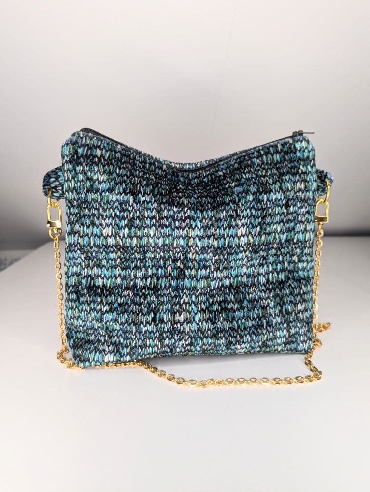 Knitted crossbody bag with a multicolored pattern in shades of blue, green, and black, featuring a gold chain strap on a white background