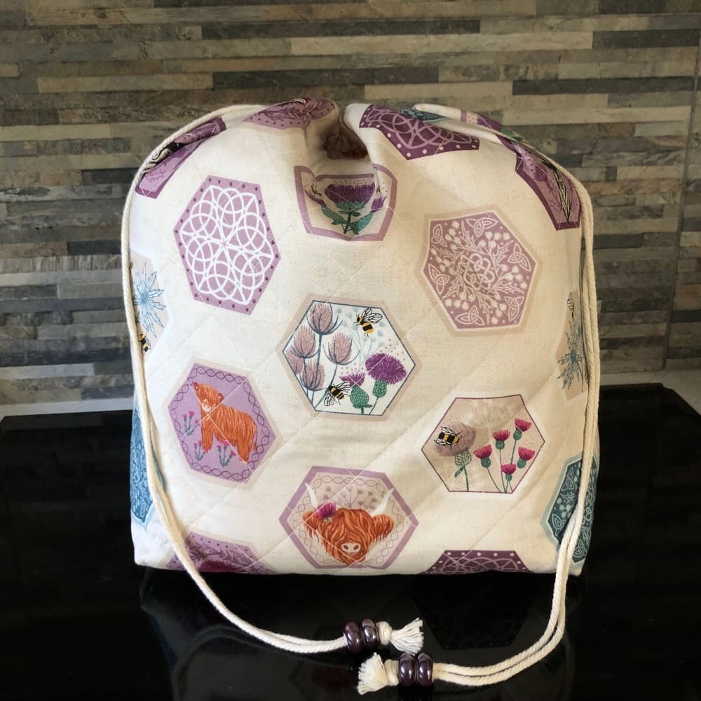 An extra large sized quilted drawstring bag in fabric featuring cute Celtic symbols. Closing using a natural cord secured by chunky shiny plum ceramic beads.