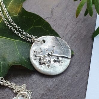 A silver pendant with an imprint of a herb