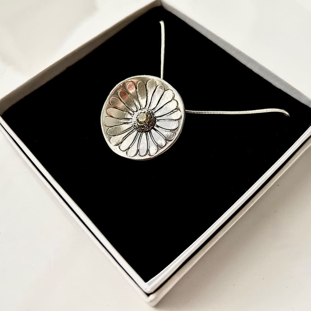 A round daisy shaped pendant with a pale yellow cubic zirconia 4mm. in the centre. It is hallmarked and has a sterling silver snake chain. It is displayed in a small white presentation box with a black velvet inlay.