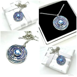 A handcrafted fine silver round shaped pendant that has a 8mm. blue cubic zirconia stone set in the centre. The pendant has been hand- painted in between the design pattern, in blue metallic points, the necklace has a sterling silver chain.