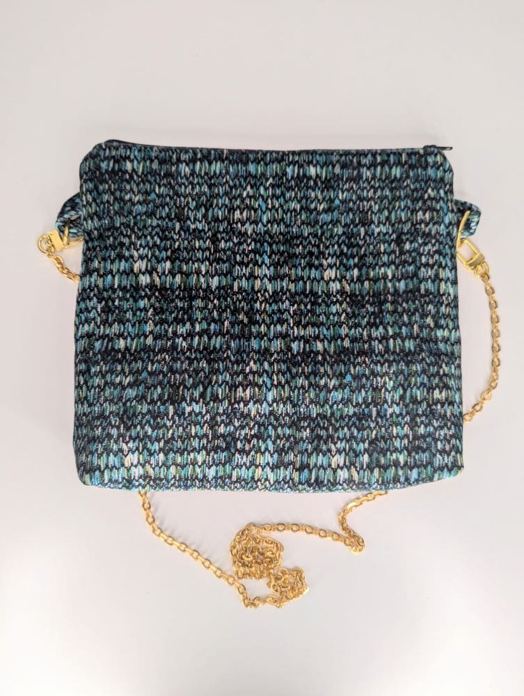 Close-up of a trendy crossbody bag showcasing a vibrant knitted pattern and elegant gold chain strap