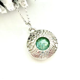 A fine silver handcrafted necklace that is round in shape with a Green fused Glass cabochon set in the centre. The pendant has a sterling silver chain.