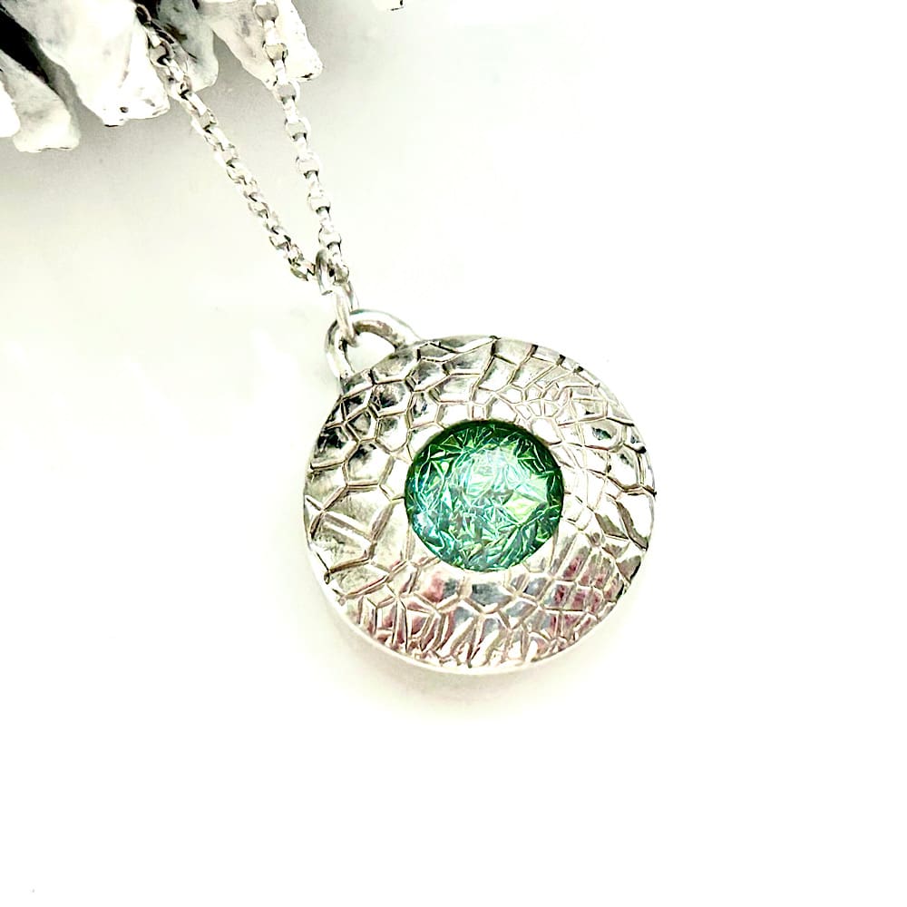 A fine silver handcrafted necklace that is round in shape with a Green fused Glass cabochon set in the centre. The pendant has a sterling silver chain.