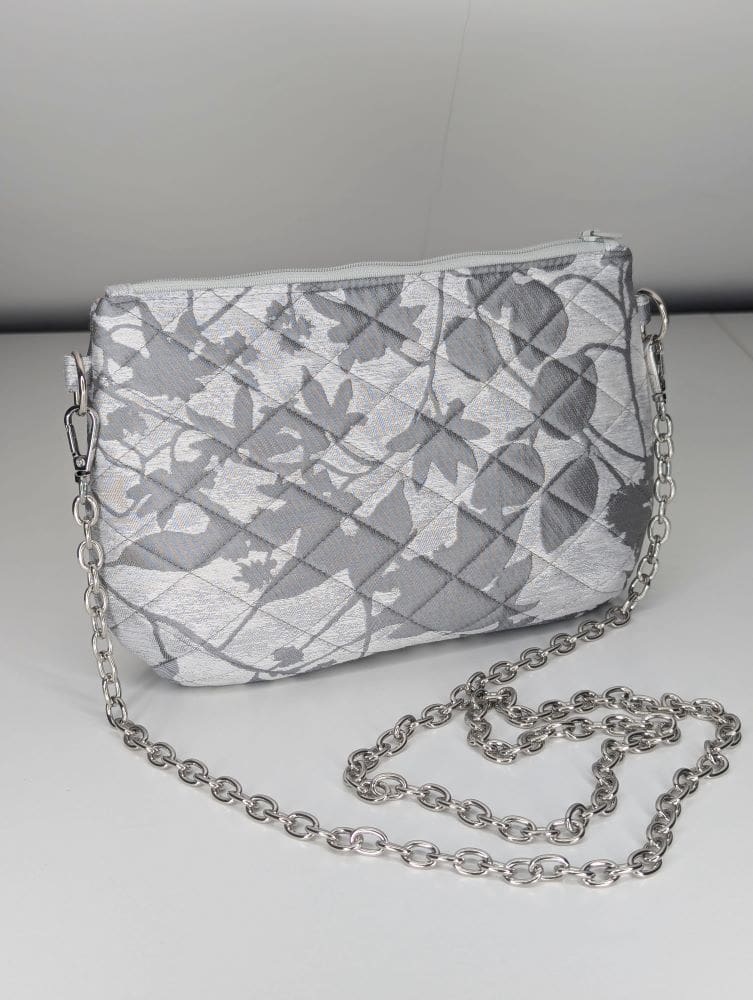 Quilted silver floral bag with a detachable chain strap on a white background