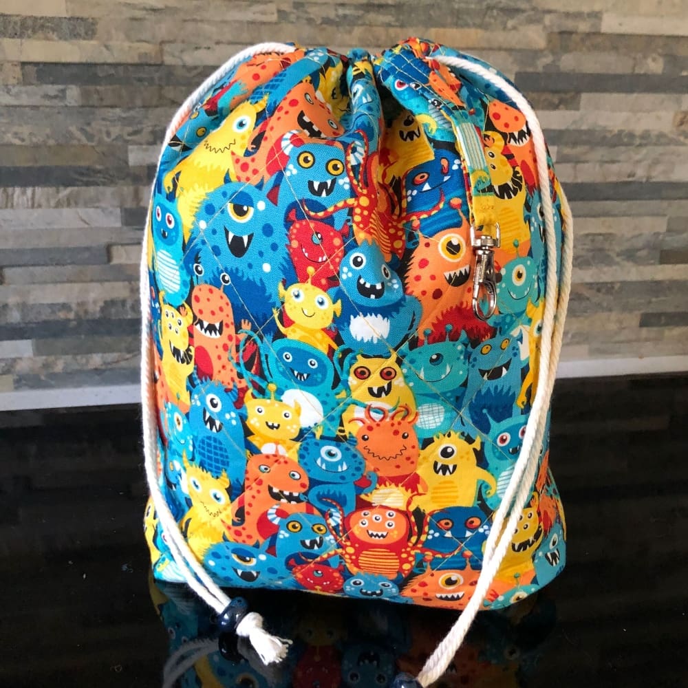 A medium sized quilted drawstring bag in blue and yellow fabric full of cute alien figures.