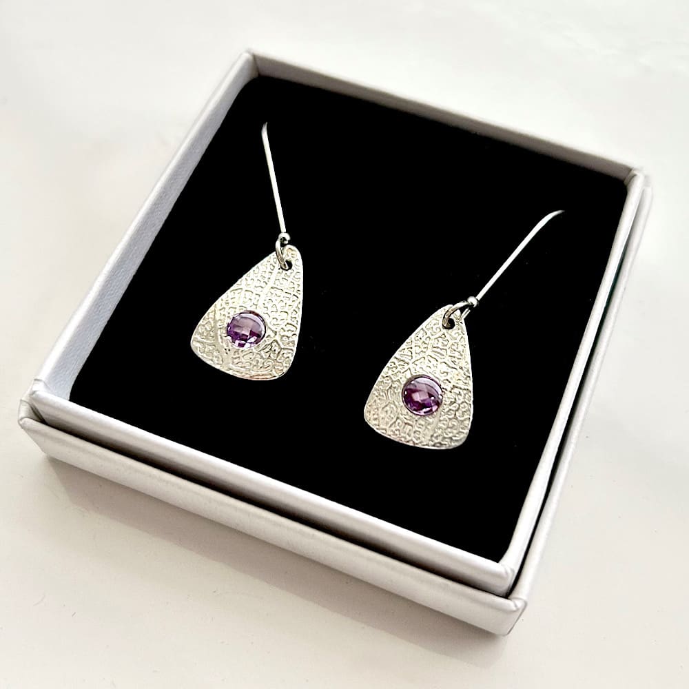 À pair of fine silver drop earrings with a amythst stone set in the centre of Rachel one. They have sterling silver ear wires and are in a white gift box with black velvet pad.