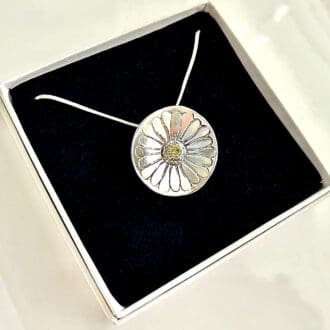 A round daisy shaped pendant with a pale yellow cubic zirconia 4mm. in the centre. It is hallmarked and has a sterling silver snake chain. It is displayed in a small white presentation box with a black velvet inlay.