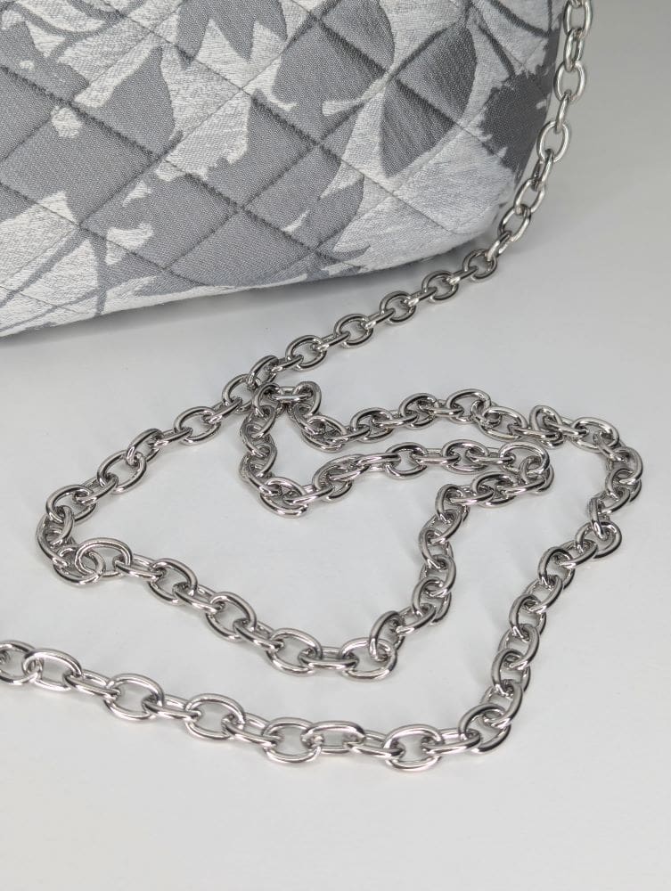 Metallic silver clutch bag with floral patterns and a chain detail.