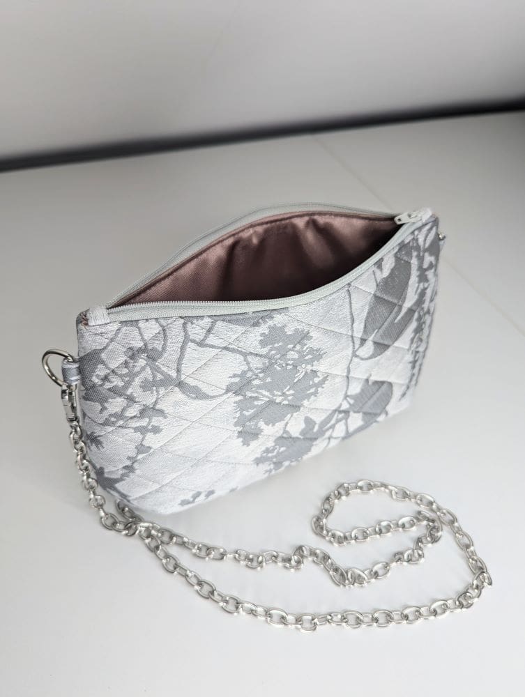 Quilted silver floral bag with a detachable chain strap on a white background.