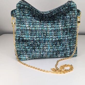 Knitted crossbody bag with a multicolored pattern in shades of blue, green, and black, featuring a gold chain strap on a white background